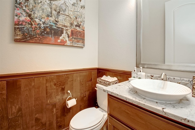 bathroom featuring vanity, wooden walls, and toilet