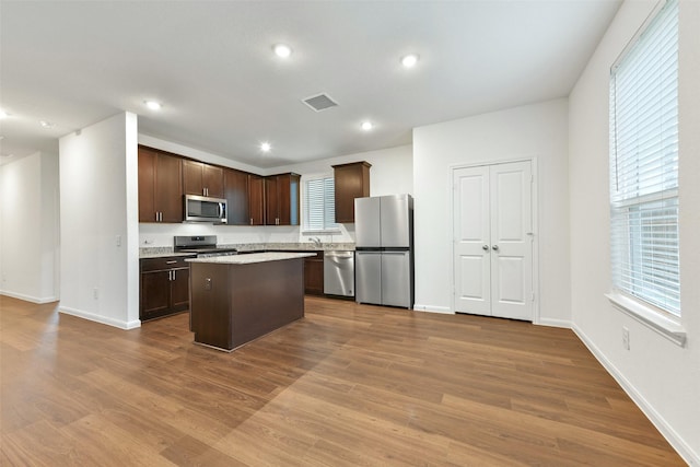 kitchen with appliances with stainless steel finishes, a center island, dark brown cabinets, and light hardwood / wood-style flooring