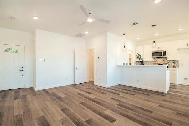 kitchen featuring dark hardwood / wood-style floors, decorative light fixtures, white cabinets, backsplash, and kitchen peninsula