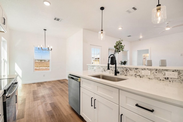 kitchen with sink, appliances with stainless steel finishes, white cabinetry, hanging light fixtures, and light wood-type flooring