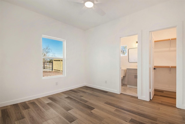 unfurnished bedroom with connected bathroom, a walk in closet, ceiling fan, dark wood-type flooring, and a closet