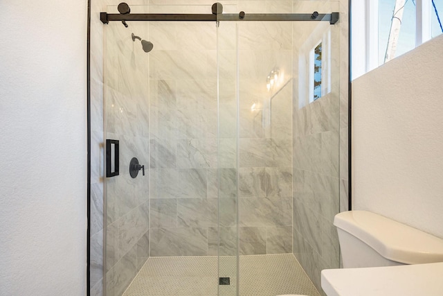 bathroom featuring a shower with door and toilet