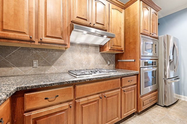 kitchen featuring built in desk, backsplash, dark stone counters, stainless steel appliances, and crown molding