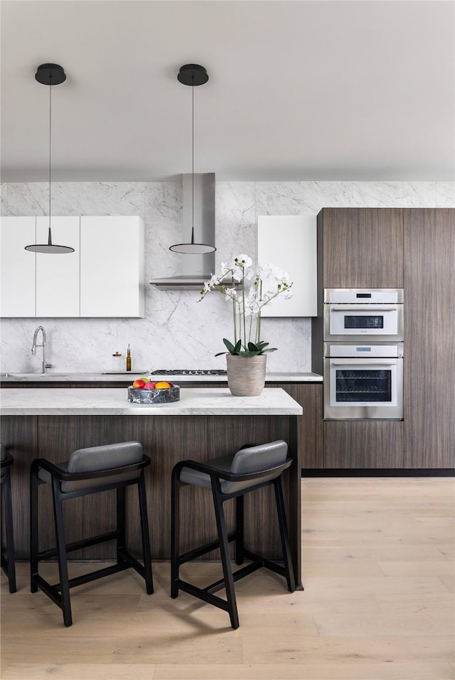kitchen featuring hanging light fixtures, white cabinetry, stainless steel double oven, and a kitchen breakfast bar