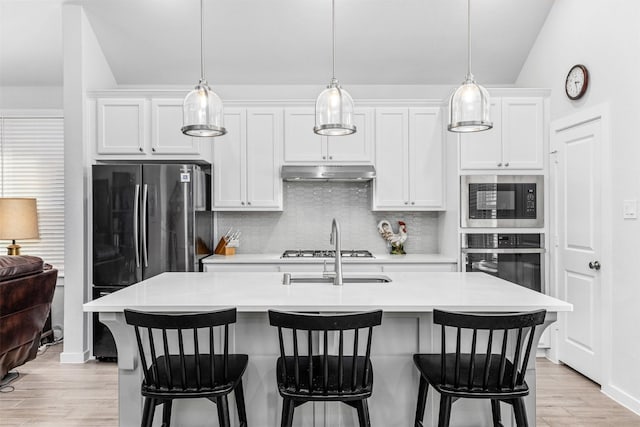 kitchen featuring white cabinetry, appliances with stainless steel finishes, an island with sink, and decorative light fixtures