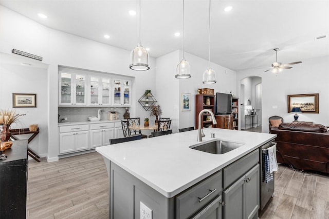 kitchen featuring sink, light hardwood / wood-style flooring, gray cabinetry, an island with sink, and decorative light fixtures