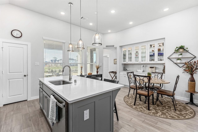 kitchen featuring gray cabinets, white cabinetry, sink, a kitchen breakfast bar, and a center island with sink