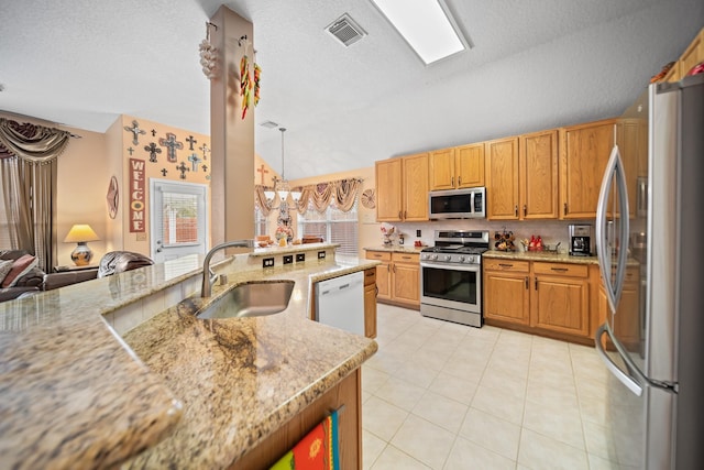 kitchen with pendant lighting, sink, appliances with stainless steel finishes, light stone countertops, and vaulted ceiling