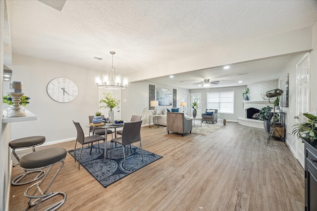 dining space with ceiling fan with notable chandelier, a textured ceiling, a fireplace, and light hardwood / wood-style flooring