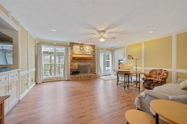 living room featuring a fireplace, ornamental molding, ceiling fan, light hardwood / wood-style floors, and a textured ceiling