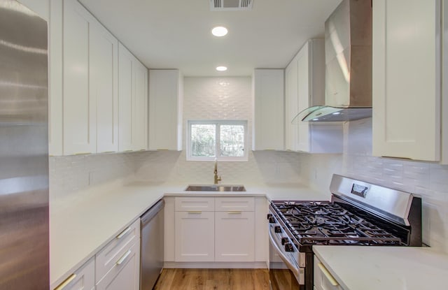 kitchen with wall chimney exhaust hood, sink, light hardwood / wood-style flooring, stainless steel appliances, and white cabinets