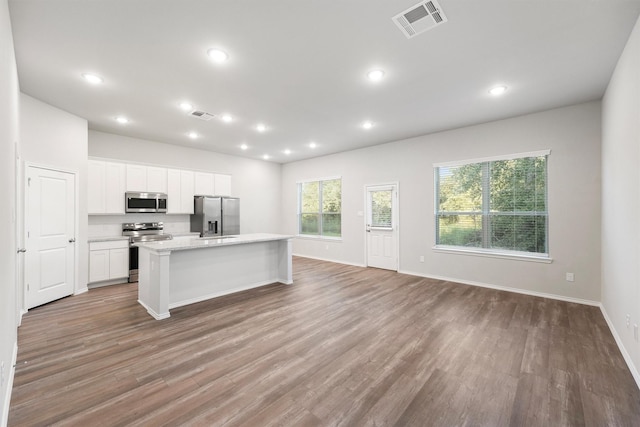 kitchen featuring hardwood / wood-style flooring, white cabinetry, stainless steel appliances, light stone counters, and an island with sink