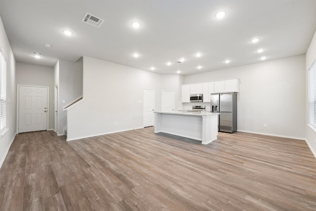 kitchen featuring appliances with stainless steel finishes, white cabinets, light stone counters, a center island with sink, and light wood-type flooring