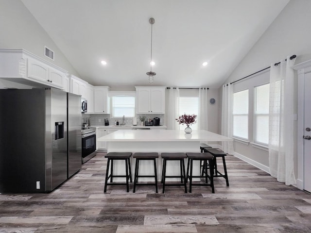 kitchen with pendant lighting, hardwood / wood-style flooring, stainless steel appliances, a center island, and white cabinets