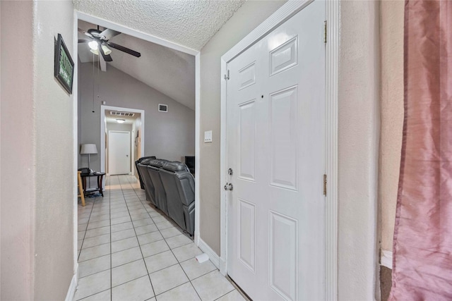 hall featuring light tile patterned floors, vaulted ceiling, and a textured ceiling