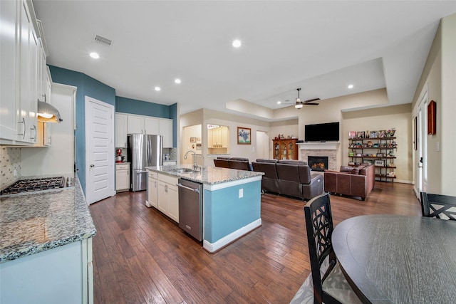 kitchen with extractor fan, white cabinetry, sink, stainless steel appliances, and a center island with sink