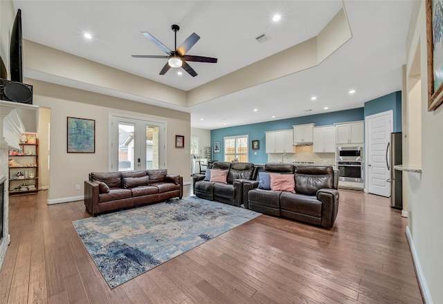 living room featuring a tray ceiling, dark wood-type flooring, ceiling fan, and french doors