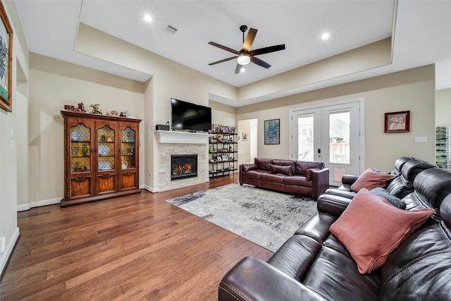 living room with ceiling fan, a stone fireplace, dark hardwood / wood-style flooring, and french doors