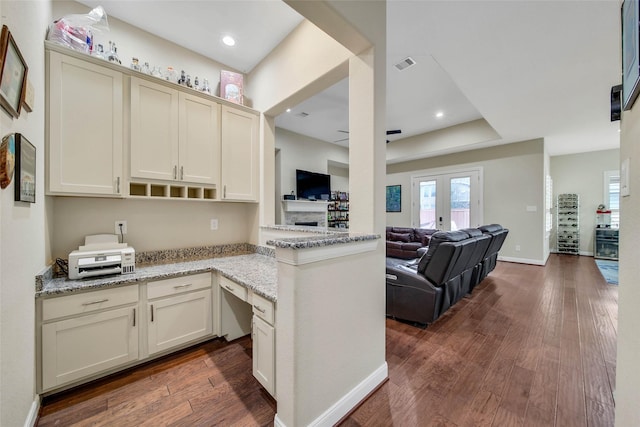 kitchen with dark hardwood / wood-style floors, cream cabinets, light stone countertops, french doors, and kitchen peninsula