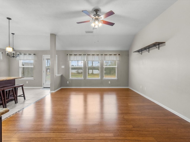 unfurnished living room featuring hardwood / wood-style flooring, vaulted ceiling, ceiling fan with notable chandelier, and a wealth of natural light