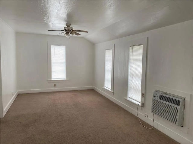 empty room featuring ceiling fan, light carpet, baseboards, vaulted ceiling, and a wall mounted air conditioner