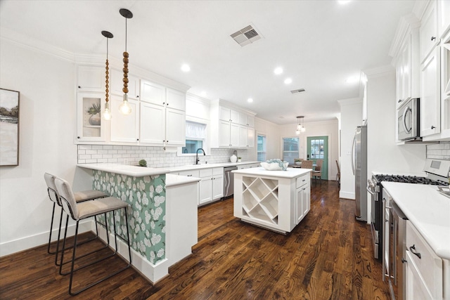 kitchen with a breakfast bar, decorative light fixtures, appliances with stainless steel finishes, kitchen peninsula, and white cabinets