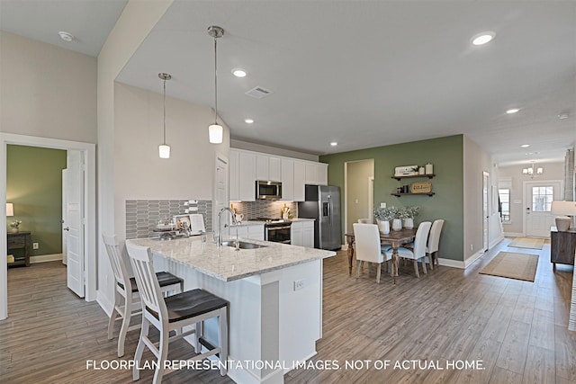 kitchen with white cabinets, appliances with stainless steel finishes, light stone counters, pendant lighting, and a sink