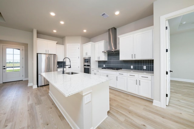 kitchen featuring sink, stainless steel appliances, white cabinets, a center island with sink, and wall chimney exhaust hood