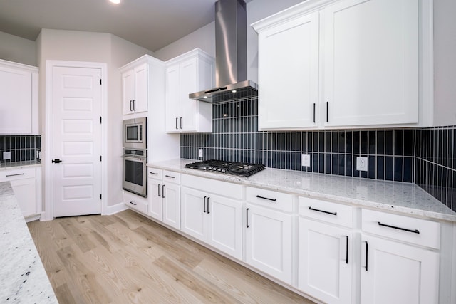 kitchen with light stone counters, appliances with stainless steel finishes, wall chimney exhaust hood, and white cabinets