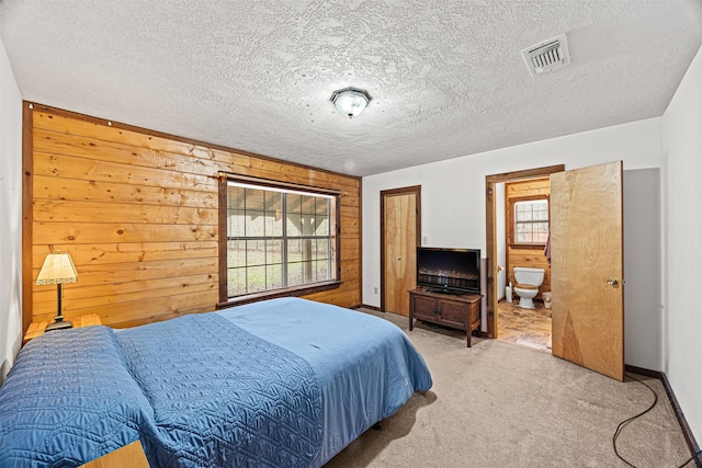 carpeted bedroom featuring ensuite bath, a textured ceiling, and wood walls