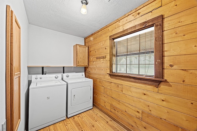 laundry area featuring cabinets, a textured ceiling, wooden walls, independent washer and dryer, and light hardwood / wood-style floors