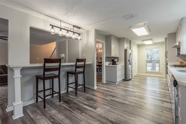 kitchen with a kitchen breakfast bar, stainless steel appliances, dark hardwood / wood-style floors, tasteful backsplash, and a textured ceiling