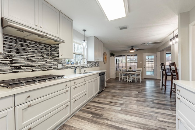 kitchen with sink, appliances with stainless steel finishes, hanging light fixtures, white cabinets, and wall chimney exhaust hood