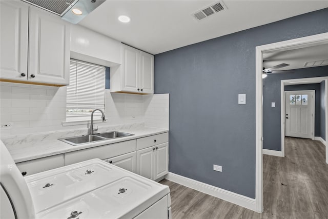 kitchen with washer / clothes dryer, sink, white cabinets, backsplash, and hardwood / wood-style flooring