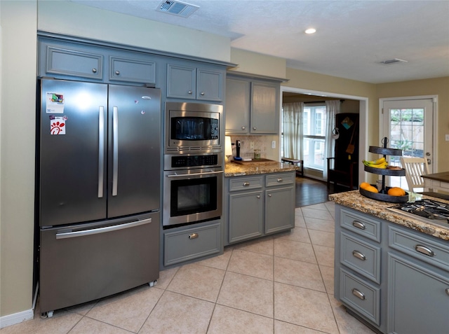 kitchen featuring gray cabinetry, stainless steel appliances, light stone counters, light tile patterned flooring, and decorative backsplash