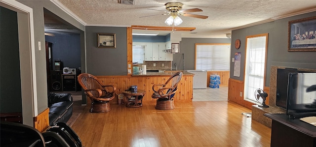 kitchen with crown molding, kitchen peninsula, light hardwood / wood-style floors, and a textured ceiling