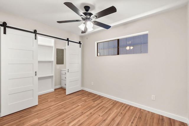 unfurnished bedroom featuring a barn door, electric panel, ceiling fan, and light hardwood / wood-style flooring