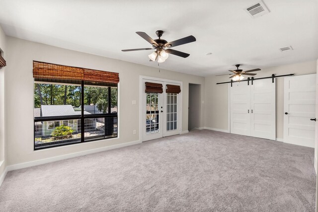 unfurnished bedroom with carpet floors, a barn door, ceiling fan, and access to outside