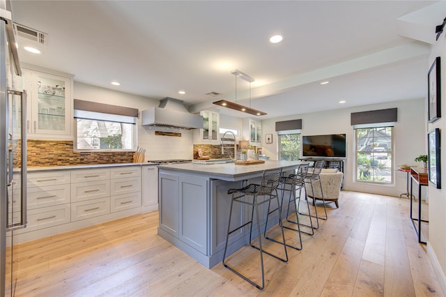 kitchen with custom exhaust hood, an island with sink, a breakfast bar area, and white cabinetry