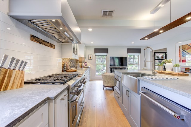 kitchen featuring light hardwood / wood-style flooring, white cabinetry, stainless steel appliances, decorative backsplash, and exhaust hood