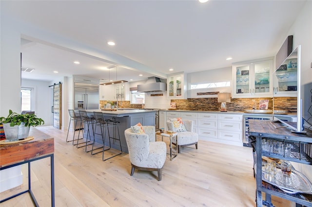 kitchen with white cabinets, a center island, stainless steel appliances, a barn door, and wall chimney range hood