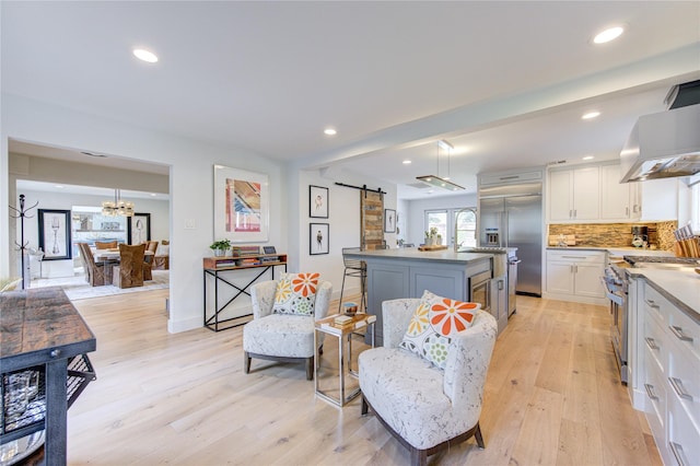 kitchen with white cabinets, premium appliances, a kitchen island with sink, a barn door, and light wood-type flooring