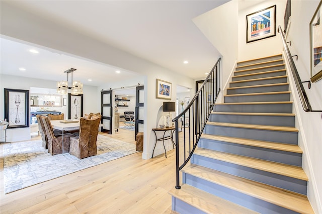 stairway featuring an inviting chandelier, hardwood / wood-style flooring, and a barn door