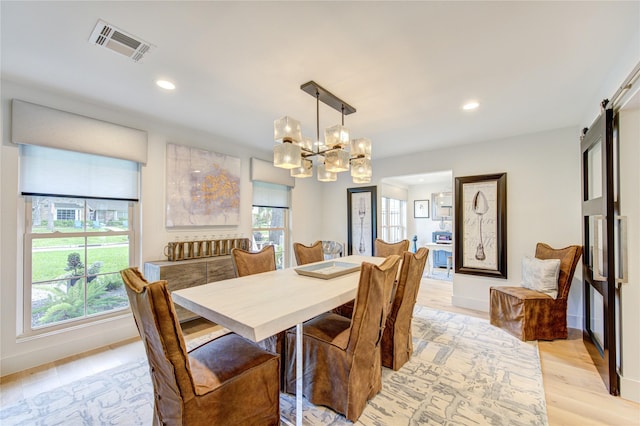 dining room featuring a barn door, an inviting chandelier, and light wood-type flooring