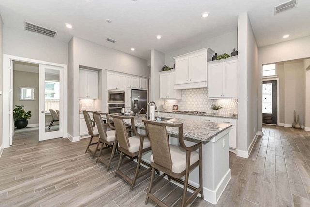 kitchen with sink, appliances with stainless steel finishes, an island with sink, white cabinets, and a kitchen bar