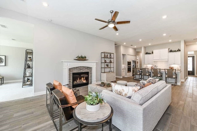 living room with a fireplace, wood-type flooring, and ceiling fan