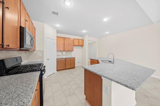 kitchen with sink, a kitchen island with sink, backsplash, light stone counters, and black range with gas stovetop