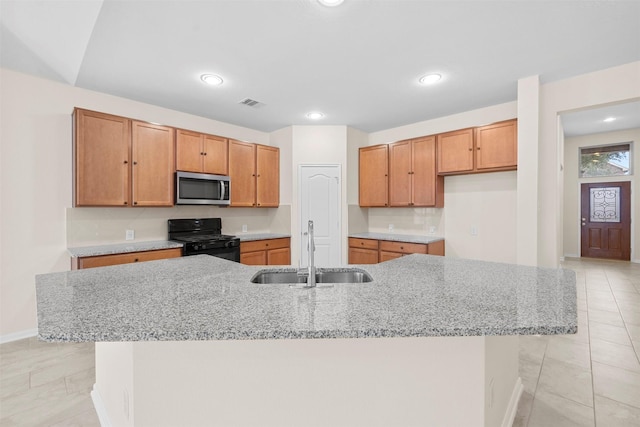 kitchen featuring sink, light stone countertops, an island with sink, and black gas stove