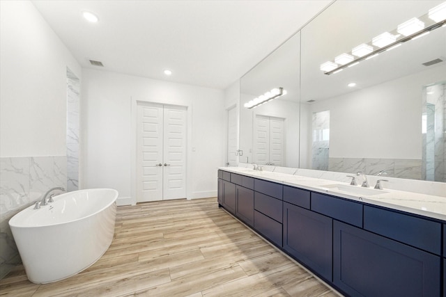 full bathroom featuring double vanity, a freestanding tub, wood finished floors, and a sink