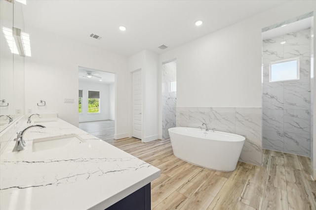 bathroom featuring a soaking tub, wood finished floors, visible vents, and a sink